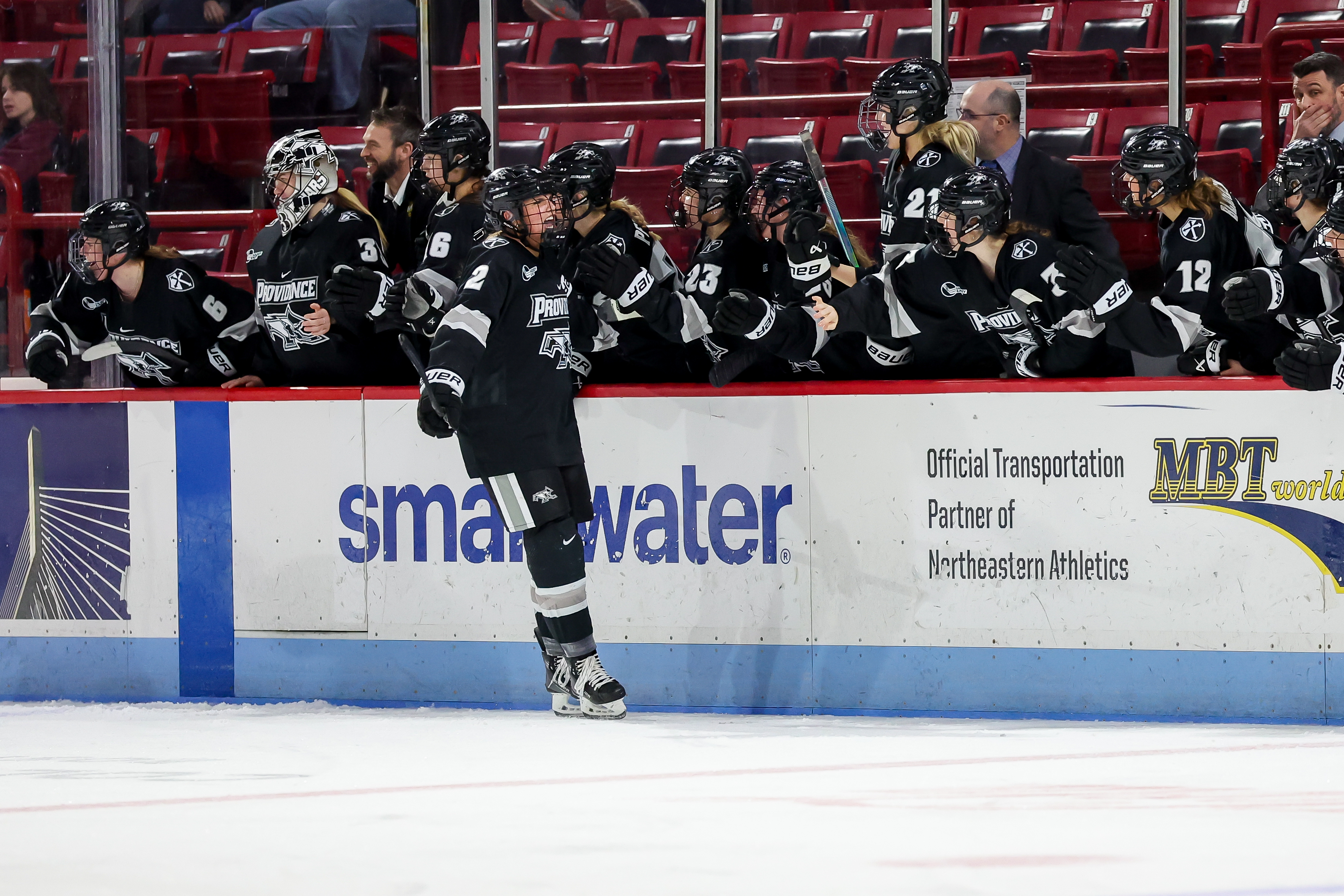 Providence women’s hockey players celebrating together at the team bench